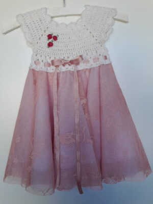 A pink baby dress with a crocheted bodice embellished with roses and ribbon waist
