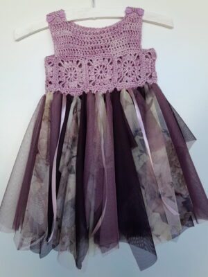 A baby dress with a granny square crocheted bodice in various shades of purple and a full tulle skirt.